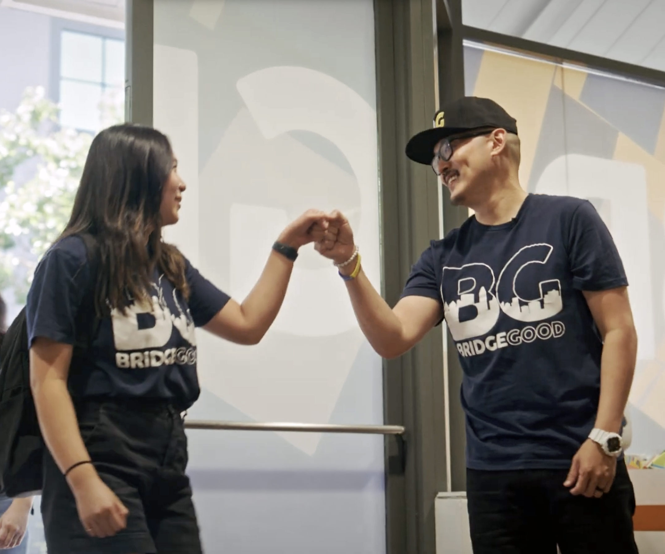 Two BRIDGEGOOD apprentices bumping fists in a bright design studio