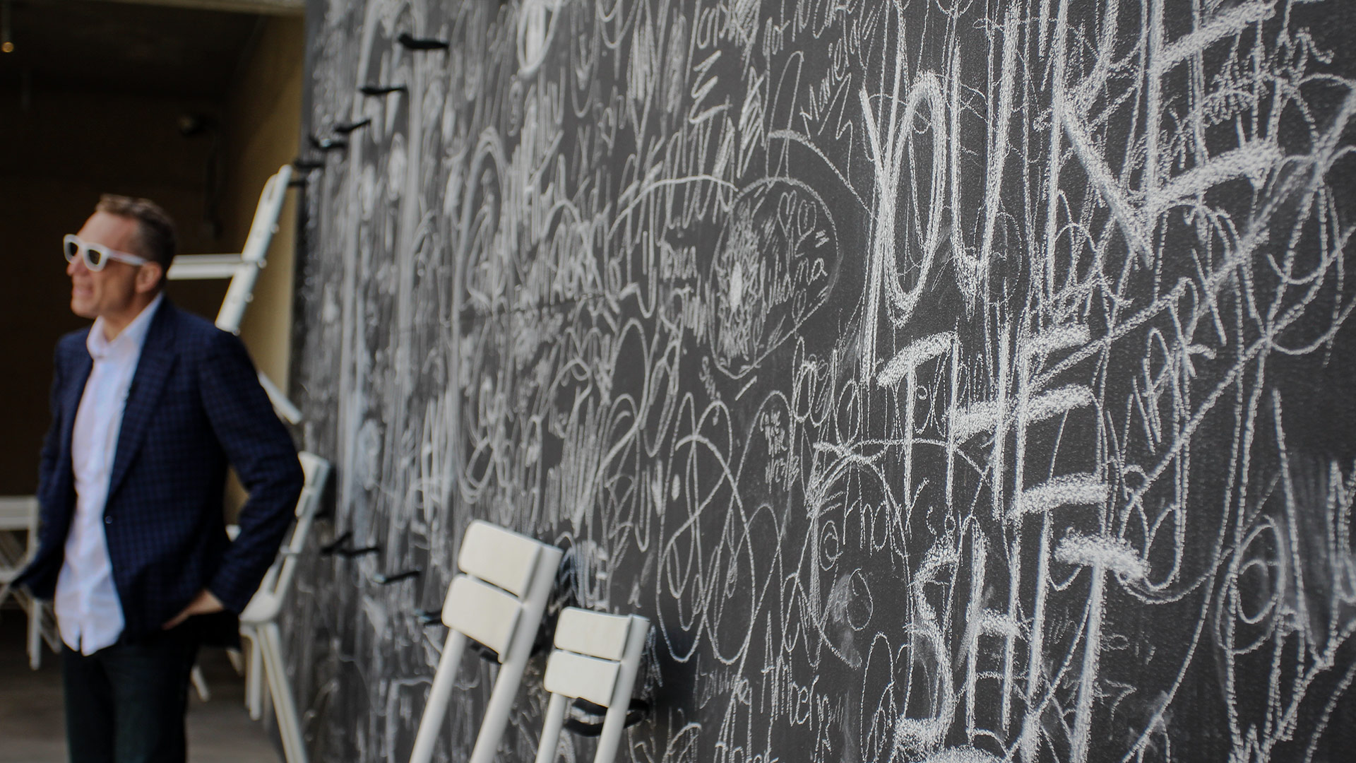 Black-and-white chalkboard wall covered in handwritten signatures and notes, with two white chairs below