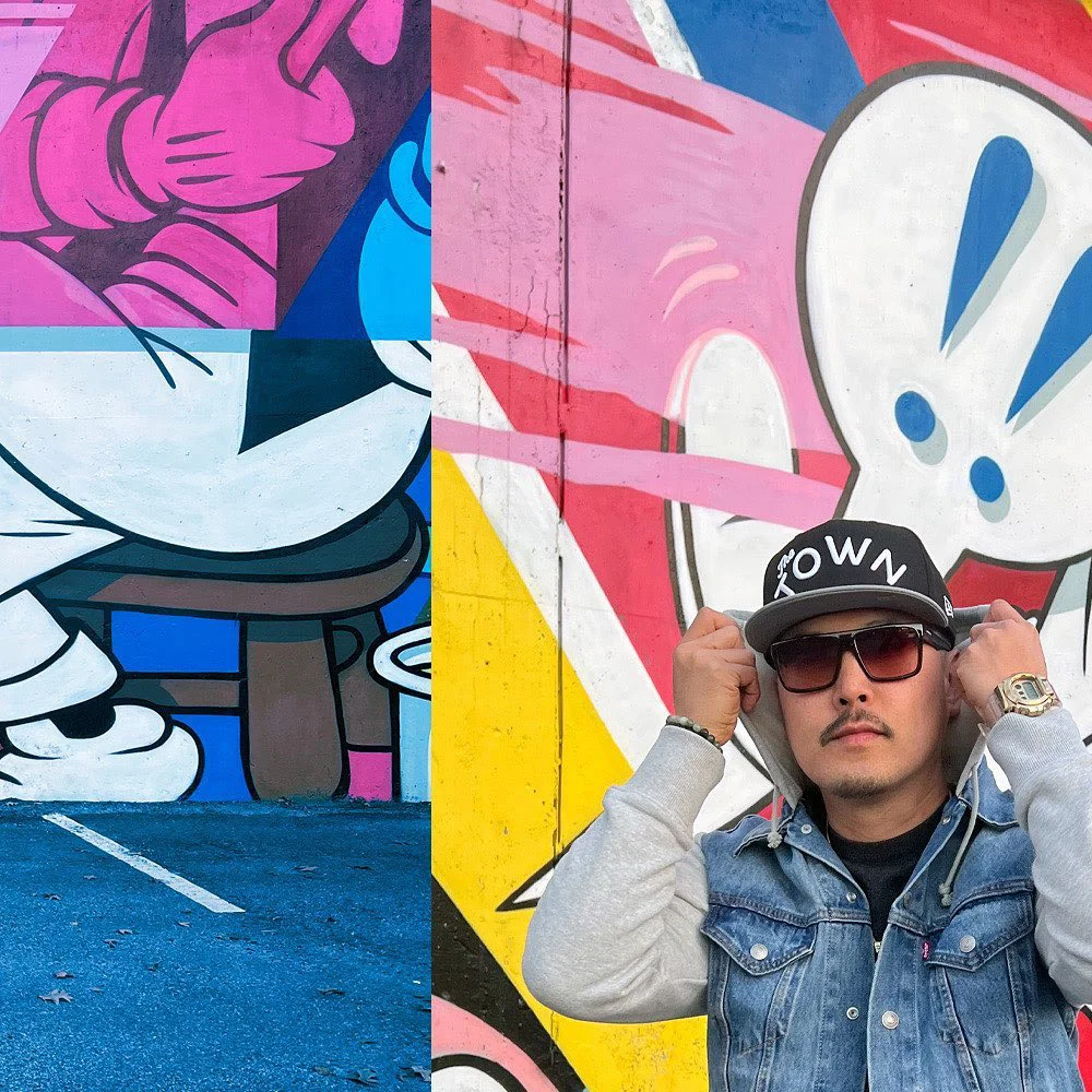 A man in sunglasses and a TOWN cap adjusts his hood in front of a bright pink, blue, and yellow cartoon mural.