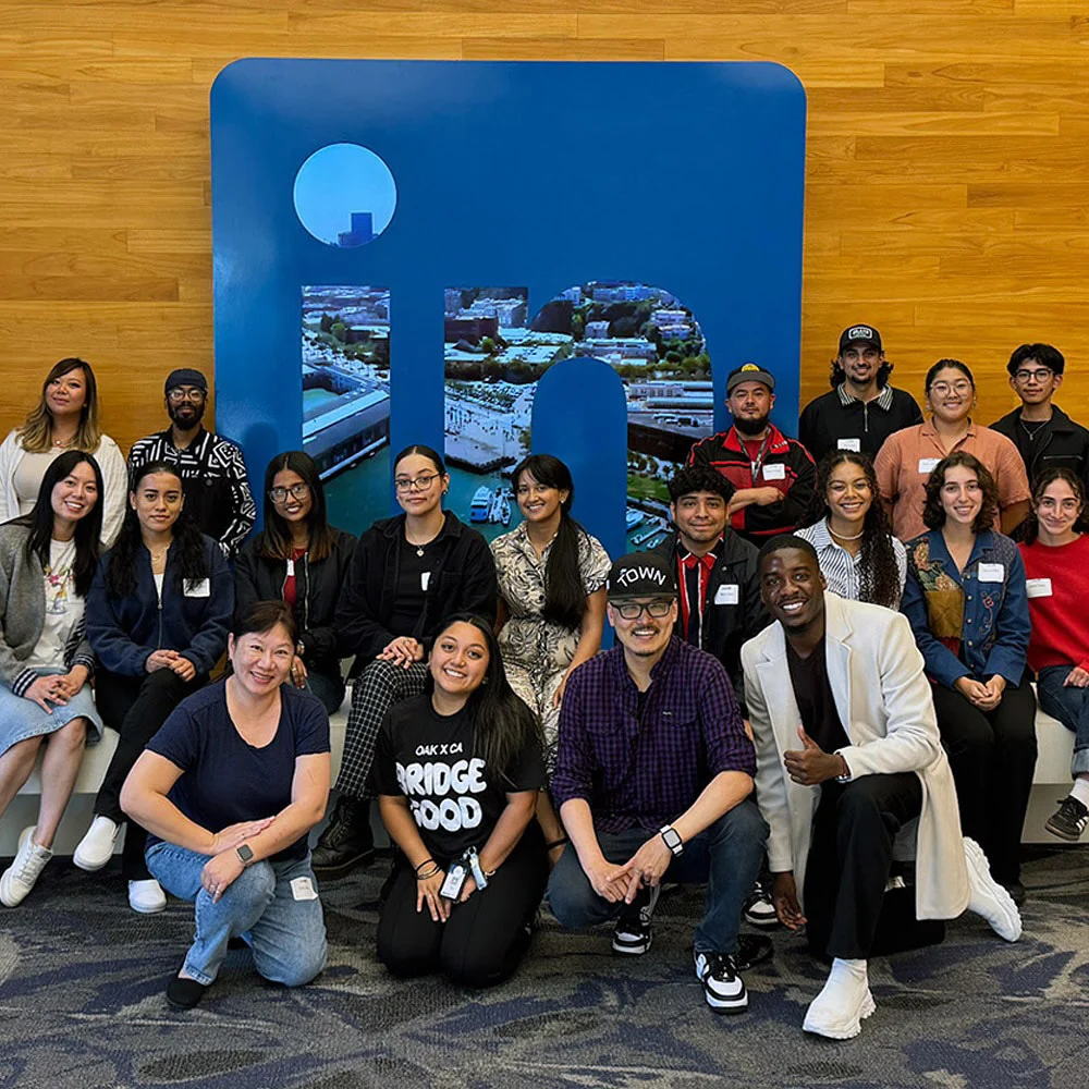 A large group poses in rows in front of a blue LinkedIn logo on a wood-paneled wall.