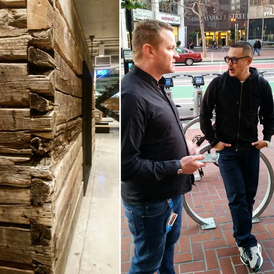 Left, stacked weathered timber beams; right, two men talking on a brick sidewalk beside a bike rack and a bike lane.