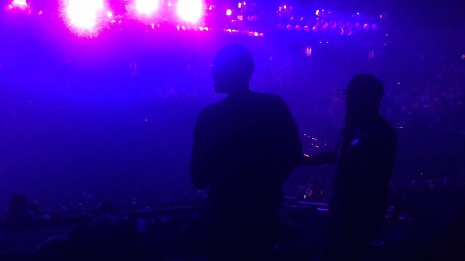 Wilson Tai (left) and Shaun Tai (right) in silhouette in a private suite at Oracle Arena, watching Drake perform under purple stage lights.