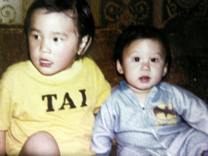 Two toddlers on a couch, one in a yellow shirt that reads TAI and one in a gray Batman sleeper.