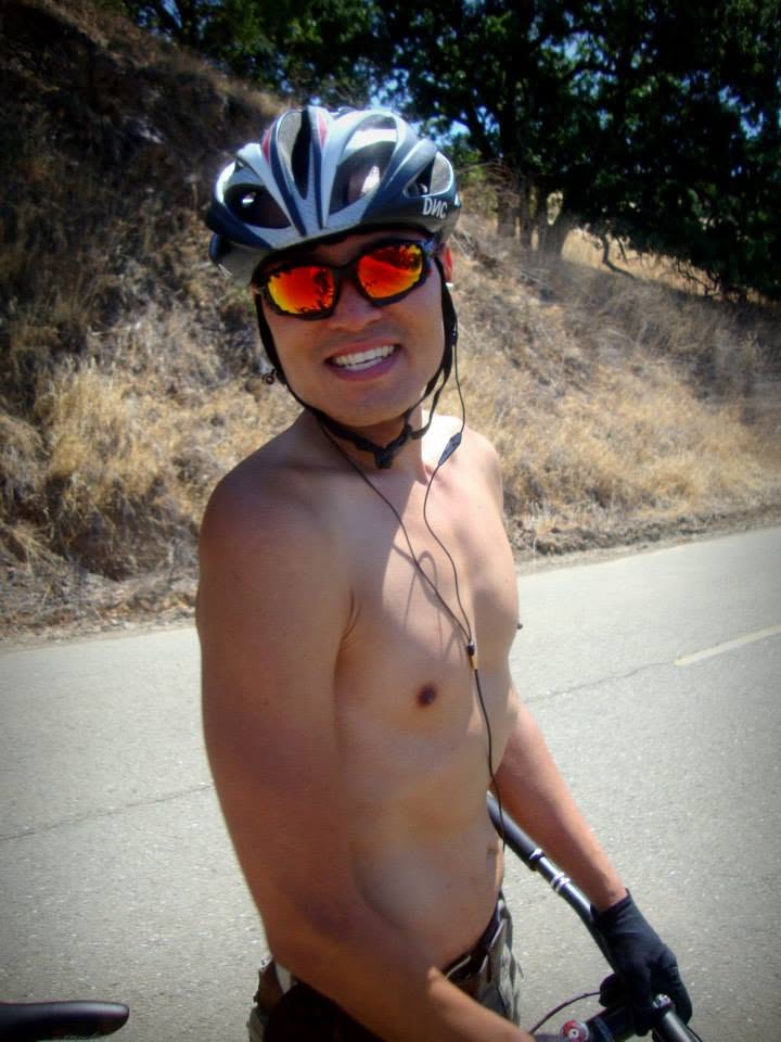Wilson Tai smiling in a cycling helmet and orange-lensed sunglasses on a country road with his bike.